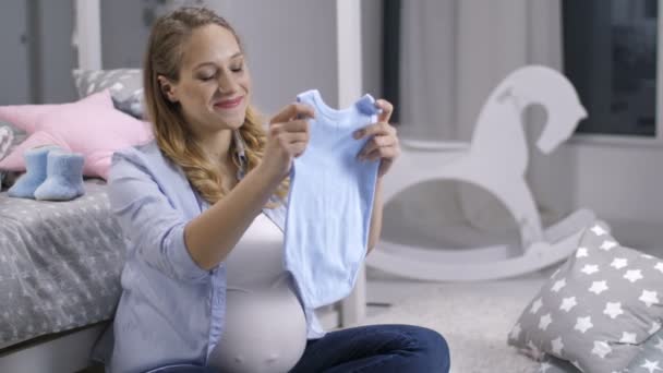 Sonriente mujer embarazada sosteniendo recién nacido onesie — Vídeo de stock