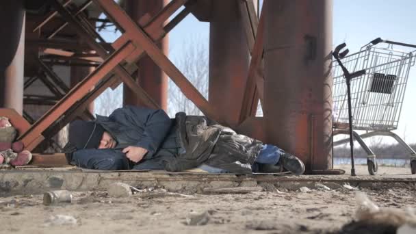 Hideg hajléktalan koldus híd alatt alszik — Stock videók