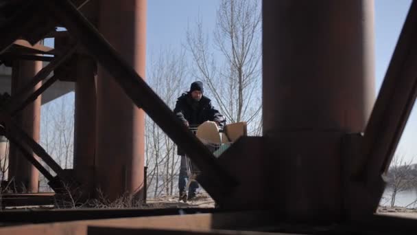 Obdachloser schubst Karren unter Brücke — Stockvideo