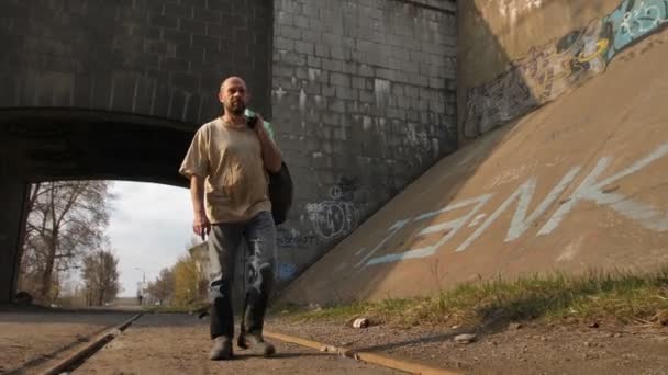 Бездомний зрілий чоловік, що йде біля мосту — стокове відео