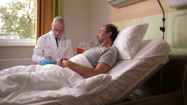 Elderly doctor talking to sick patient in bed — Stock Video