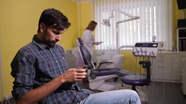 Klient korzystający z telefonu czeka na wizytę u dentysty — Wideo stockowe