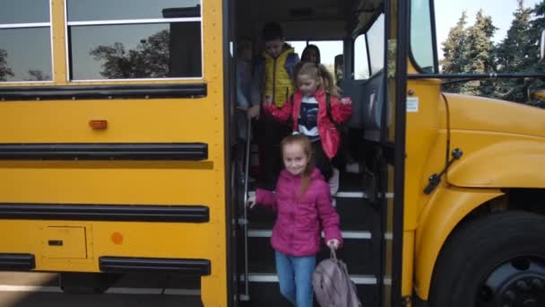 Små elever kliver av bussen och går i skolan — Stockvideo