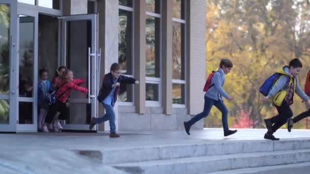 Веселые школьники начального возраста покидают школу — стоковое видео