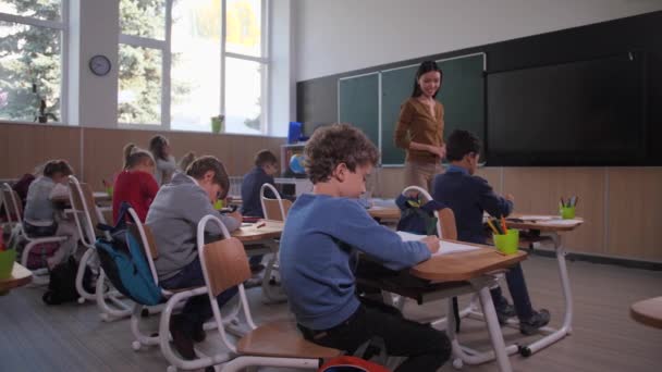 Жінка вчителька цікавиться малюванням школяра — стокове відео