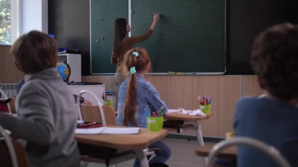 Vrouwelijke leraar schrijven wiskunde equatian op schoolbord — Stockvideo