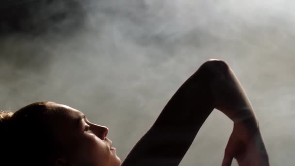 Молодой танцор делает движение руками в дымчатой студии — стоковое видео