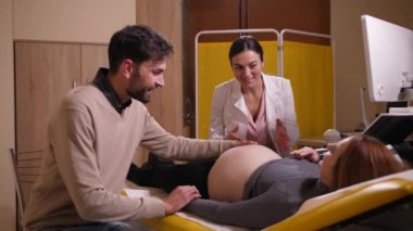 Happy man stroking pregnant wifes belly in clinic