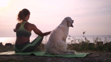 Sağlıklı bir kadın kıyıda köpeğin yanında meditasyon yapıyor.