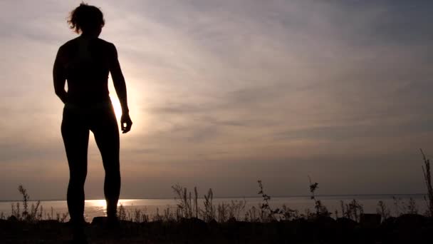 Silhouet van fitte vrouw genietend van zonsondergang aan wal — Stockvideo