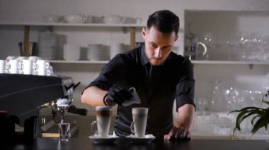 Barista bir bardak kremalı sütü kahveyle dolduruyor.