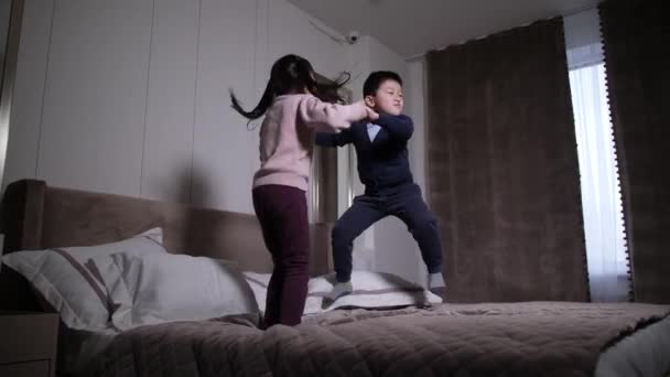 Щасливі азіатські діти розважаються стрибаючи на ліжку вдома — стокове відео