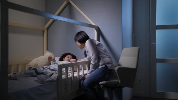 Заботливая китайская мама укладывает маленькую дочь спать — стоковое видео