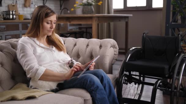 Женщина-инвалид работает на планшете сидя на диване — стоковое видео