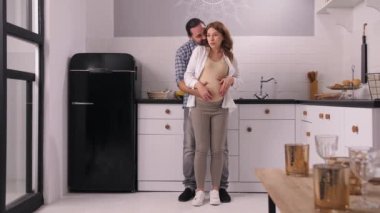 Neşeli hamile çift mutfakta karnını okşuyor.