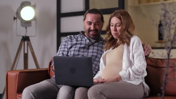 Радостная беременная пара смотрит комедию дома — стоковое видео
