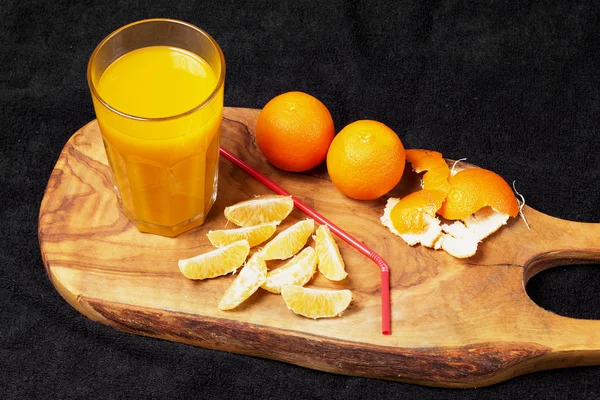 Several mature citrus and a glass of juice on a wooden table on a blackboard - mandarins — Stock Photo, Image