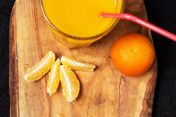 Mehrere reife Zitrusfrüchte und ein Glas Saft auf einem Holztisch auf einer Tafel - Mandarinen — Stockfoto