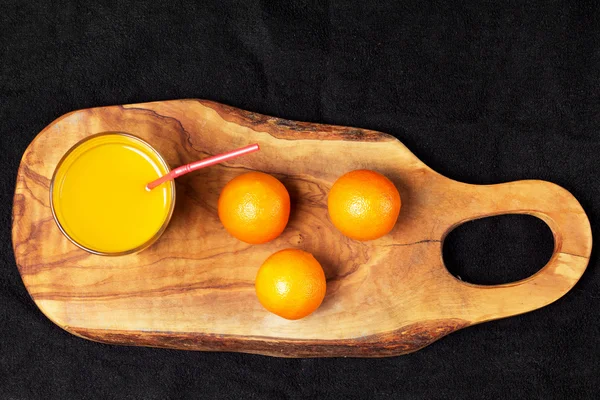 Several mature citrus and a glass of juice on a wooden table on a blackboard - mandarins — Stock Photo, Image