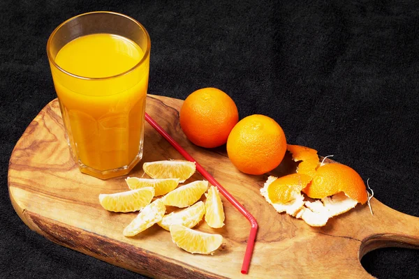 Vários cítricos maduros e um copo de suco em uma mesa de madeira em um quadro-negro - mandarinas — Fotografia de Stock