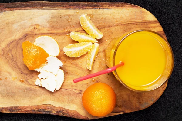 Mehrere reife Zitrusfrüchte und ein Glas Saft auf einem Holztisch auf einer Tafel - Mandarinen — Stockfoto