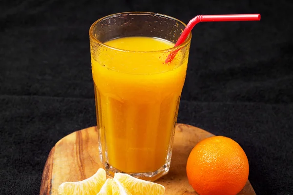 Mehrere reife Zitrusfrüchte und ein Glas Saft auf einem Holztisch auf einer Tafel - Mandarinen — Stockfoto