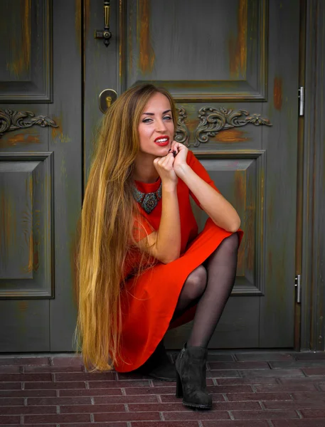 Модная молодая девушка на фоне старинной двери в красном платье с длинными волосами — стоковое фото