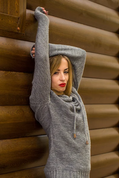 Bella ragazza in un maglione con i capelli lunghi e labbra rosse sullo sfondo di tronchi di legno — Foto Stock