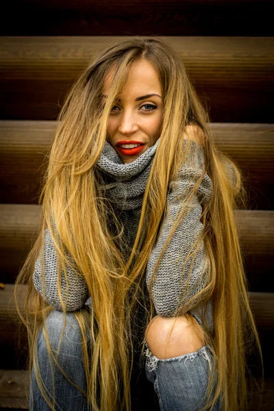 Красивая девушка в свитере с длинными волосами и красными губами на фоне деревянных бревен — стоковое фото