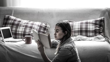 Beyaz rahat yatak ve sıcak bir içecek, ev kavramlarını ve konfor içme güzel bir kız ile bir bilgisayar ve bir kitap