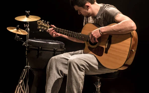 Musicien joue de la guitare acoustique et des instruments de percussion, fond noir — Photo