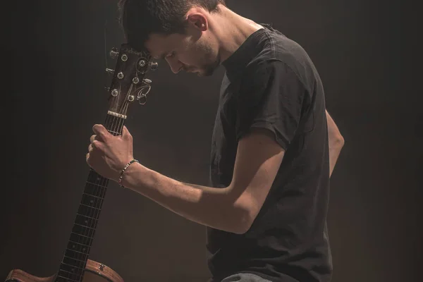 Jeune homme avec guitare acoustique sur fond noir — Photo