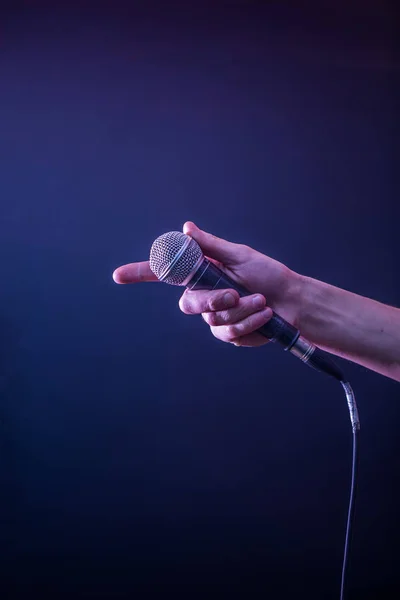 Ręka z mikrofonem na czarnym tle, koncepcja muzyka, piękne oświetlenie na scenie — Zdjęcie stockowe