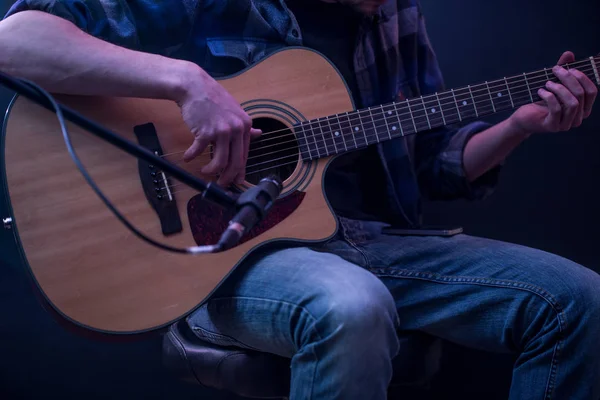 Homem tocando guitarra acústica em um fundo preto, o conceito de música, bela iluminação no palco — Fotografia de Stock