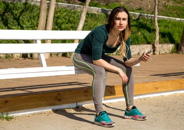The girl in sportswear on a bench listening to music — Stock Photo, Image
