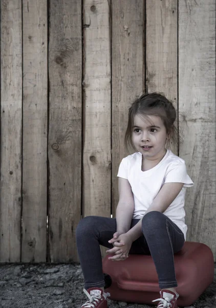 Маленькая девочка сидит на деревянном фоне — стоковое фото