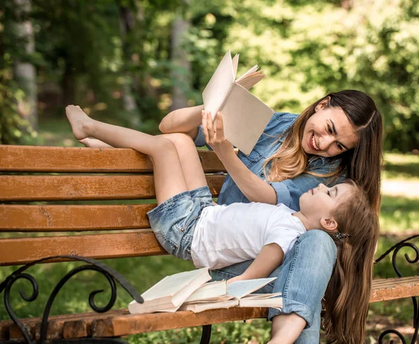 Мама и дочь на скамейке запасных читают книгу — стоковое фото
