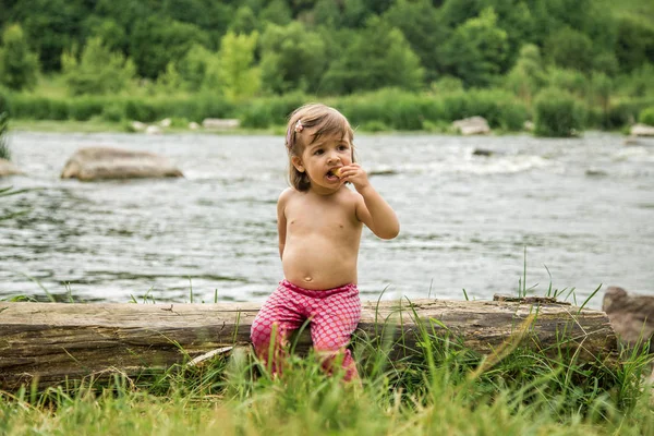 Niña sentada en un tronco cerca del río — Foto de Stock