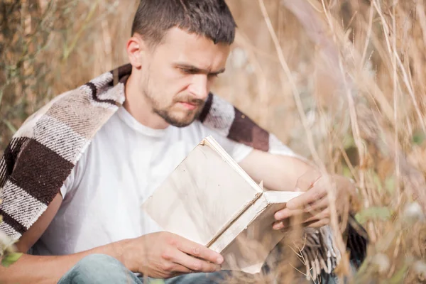 Um jovem no campo lendo um livro — Fotografia de Stock