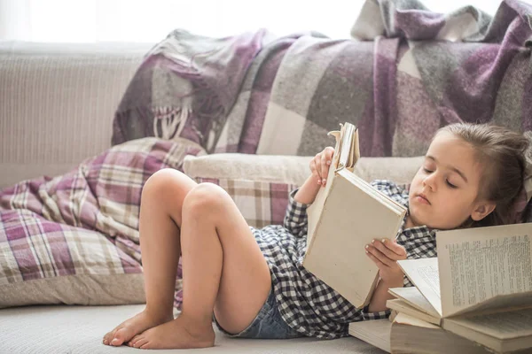 Malá holčička čtení knihy na pohovce — Stock fotografie