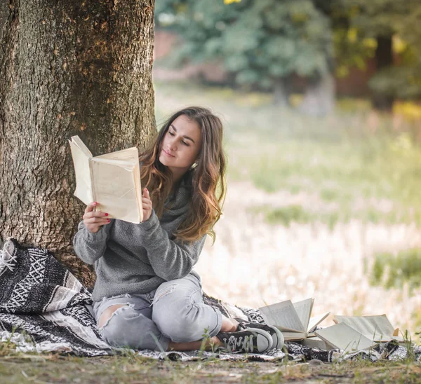 Egy fiatal lány, egy fa, egy könyvet olvas közelében — Stock Fotó