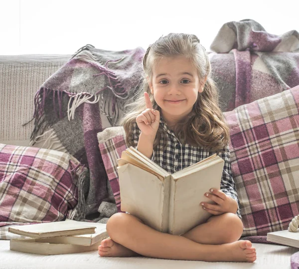 Kislány könyvével a kanapé — Stock Fotó