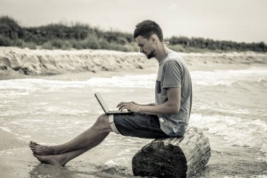 bilgisayar ile plajda çalışan adam