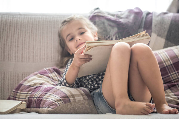 little girl reading book on sofa