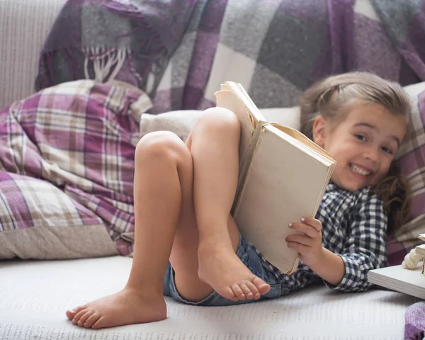 Kleines Mädchen liest Buch auf dem Sofa — Stockfoto