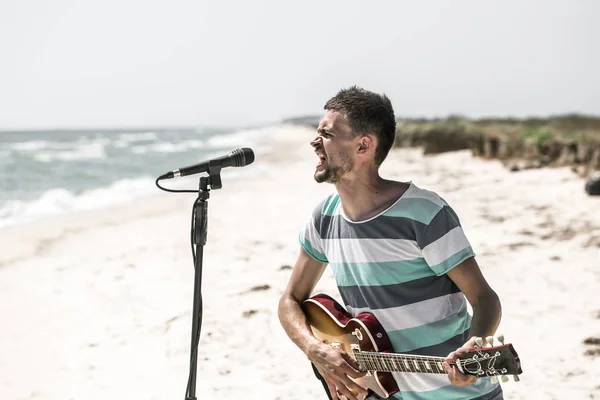 Βράχο στην παραλία, ο μουσικός να παίζει κιθάρα και να τραγουδάει στο μικρόφωνο, η έννοια του ελεύθερου χρόνου και τη δημιουργικότητα — Φωτογραφία Αρχείου