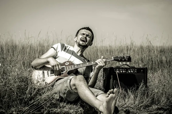 Ο νεαρός άνδρας στο πεδίο, ο μουσικός με την κιθάρα και ενισχυτή, η έννοια της μουσικής και της τέχνης — Φωτογραφία Αρχείου