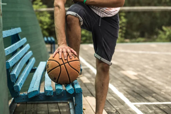 Jovem jogador de basquete feliz sentado no parque com uma toalha