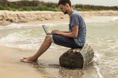 bilgisayar ile plajda çalışan adam