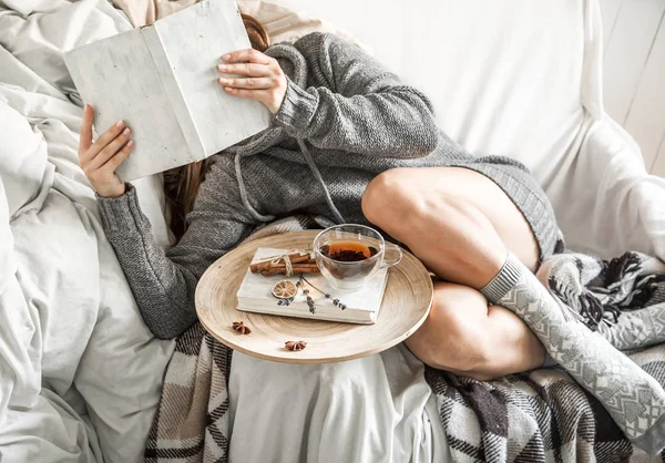 La muchacha en el sofá con el té y el libro — Foto de Stock